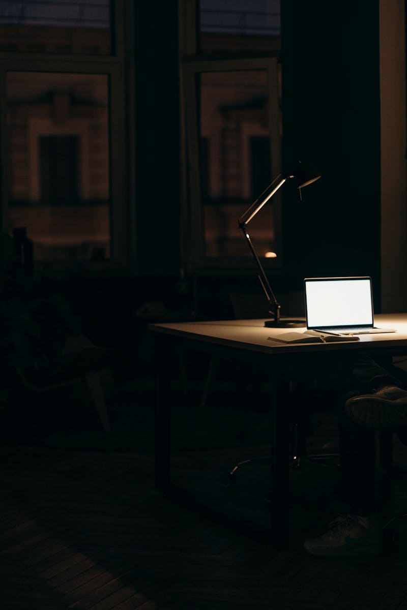 A man working late at night in a dimly lit office, with a bright laptop screen.